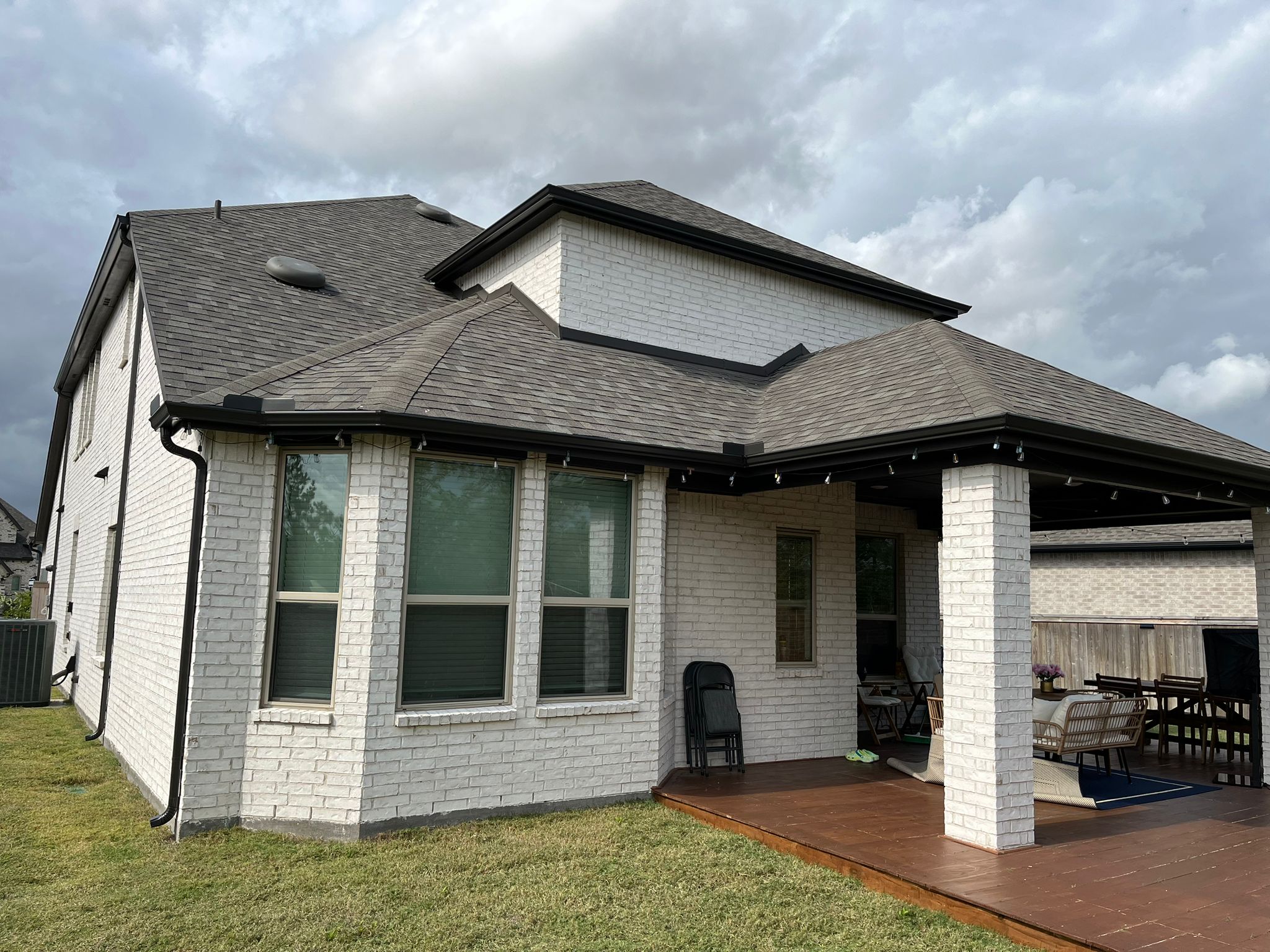 Finished white brick home with black seamless gutters and a covered patio